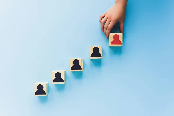 Partial view of hand and wooden blocks with black and red human icons on blue background, leadership concept — Stock Photo