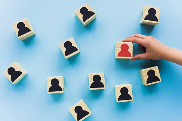 Vista parcial de la mano sosteniendo bloque de madera con icono humano rojo sobre fondo azul, concepto de liderazgo - foto de stock