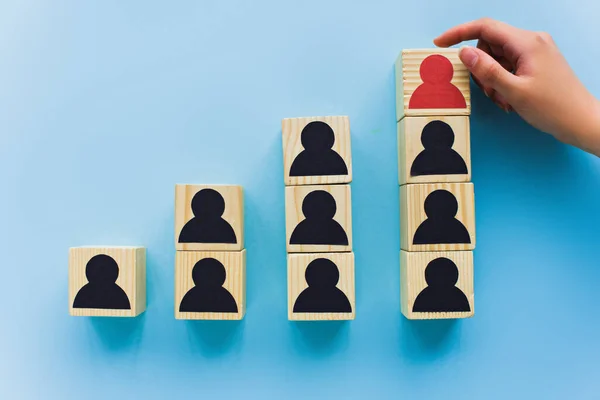 Vista parcial de la mano cerca de bloques de madera con iconos humanos negros y rojos sobre fondo azul, liderazgo y concepto de escalera de carrera - foto de stock