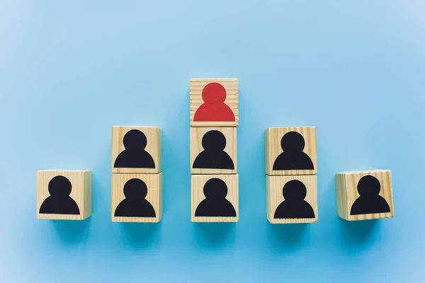 Vista dall'alto di blocchi di legno con icone umane nere e rosse su sfondo blu, concetto di leadership e carriera — Foto stock