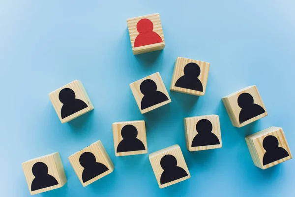 Vista superior de bloques de madera con iconos humanos negros y rojos dispersos sobre fondo azul, concepto de liderazgo - foto de stock