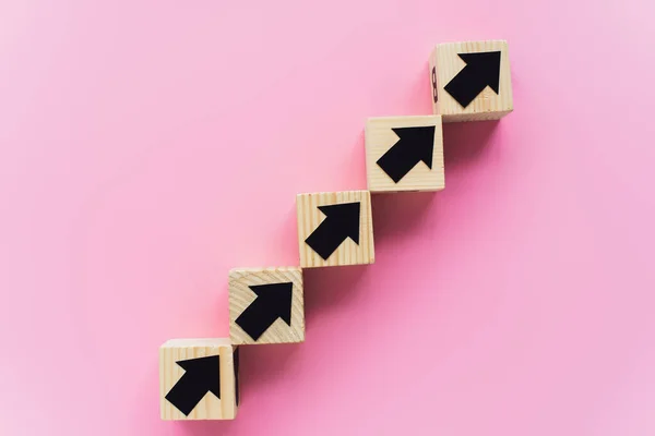 Vista dall'alto di blocchi di legno con frecce nere su sfondo rosa, concetto di business — Foto stock