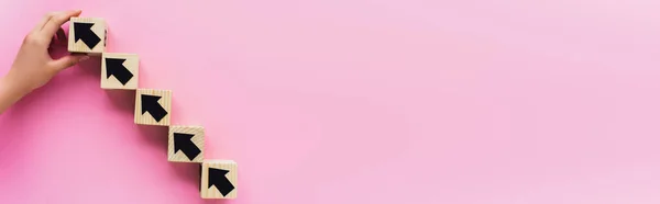 Vista parcial de la mano cerca de bloques de madera con flechas negras sobre fondo rosa, concepto de negocio - foto de stock