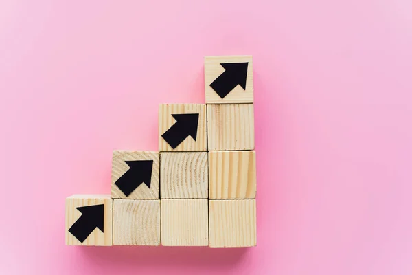 Vista dall'alto di blocchi di legno con frecce nere su sfondo rosa, concetto di business — Foto stock