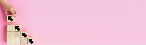 Vista parcial de la mano cerca de bloques de madera con flechas negras sobre fondo rosa, concepto de negocio — Stock Photo