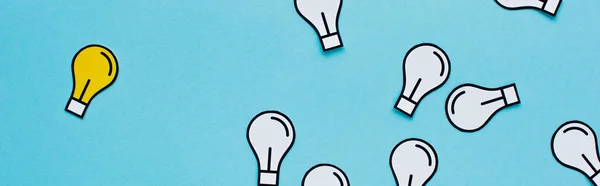 Panoramic shot of paper light bulbs scattered on blue background, business concept — Stock Photo