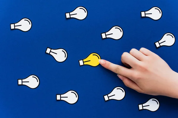 Vista recortada de la mano apuntando a la bombilla de papel sobre fondo azul, concepto de negocio - foto de stock