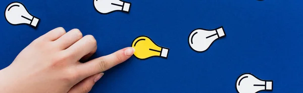 Cropped view of hand pointing at paper light bulb on blue background, business concept — Stock Photo