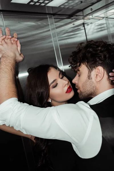 Beau homme embrassant belle femme avec des lèvres rouges dans l'ascenseur — Photo de stock