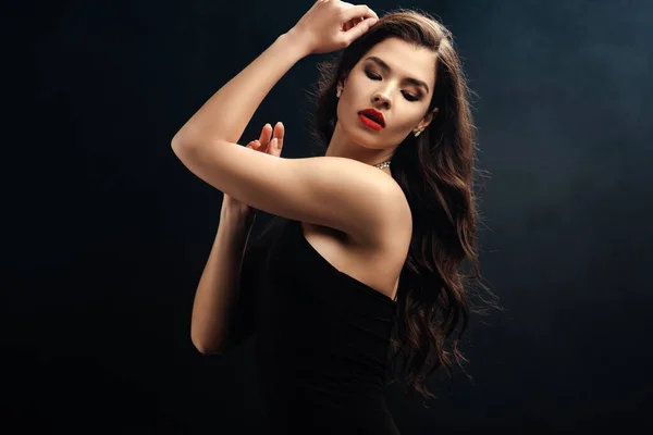 Hermosa mujer en vestido negro con labios rojos sobre fondo negro - foto de stock