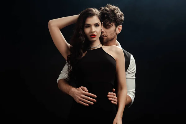 Hombre guapo abrazando a mujer hermosa con labios rojos aislados en negro - foto de stock