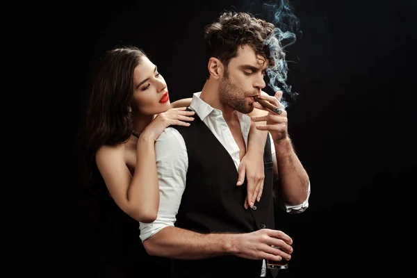 Belle fille embrassant petit ami avec verre de whisky et cigare isolé sur noir — Photo de stock