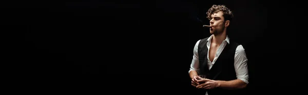 Панорамна орієнтація красивого чоловіка у формальному носінні курильної сигари та склянки віскі ізольовані на чорному — стокове фото