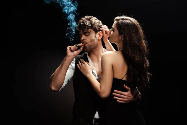 Homem fumando charuto e abraçando namorada no fundo preto — Fotografia de Stock
