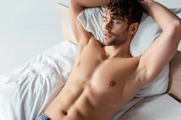 Hombre musculoso guapo mirando hacia otro lado en la cama aislado en blanco - foto de stock