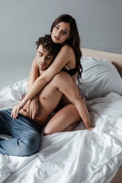 Sensual mujer abrazando sin camisa novio en la cama aislado en gris - foto de stock