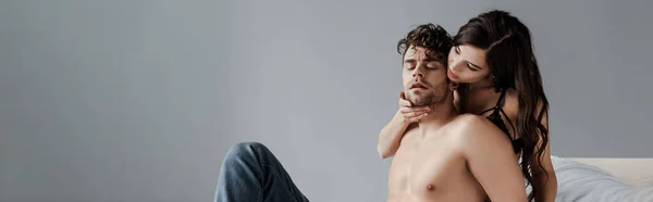 Foto panorámica de mujer tocando barbilla de novio sin camisa en la cama sobre fondo gris - foto de stock