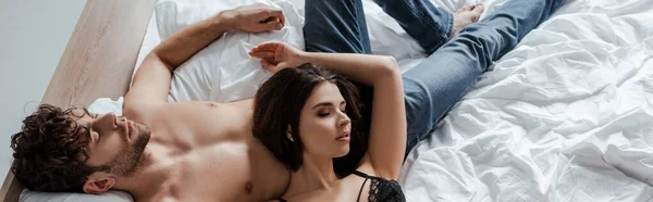 Panorâmica tiro de mulher sexy deitado no muscular namorado em jeans na cama — Fotografia de Stock