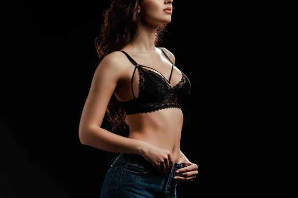 Vue recadrée de la femme en soutien-gorge en dentelle toucher jeans isolé sur noir — Photo de stock