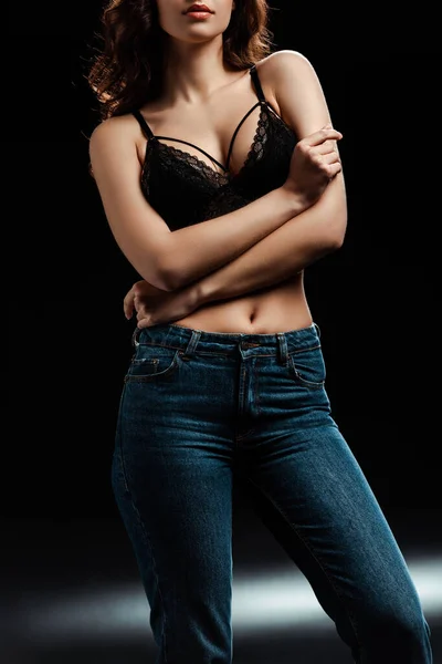 Cropped view of woman in lace bra and jeans on black background — Stock Photo