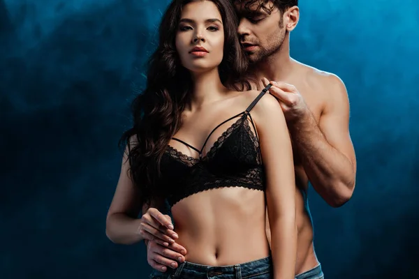 Shirtless man touching bra of beautiful brunette woman on black background with smoke — Stock Photo