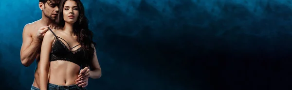 Панорамний знімок без сорочки, який обіймає і зворушливий бюстгальтер сексуальної жінки на чорному тлі з димом — стокове фото