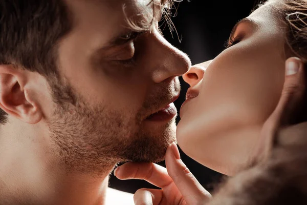 Enfoque selectivo de la mujer joven besar novio guapo aislado en negro - foto de stock