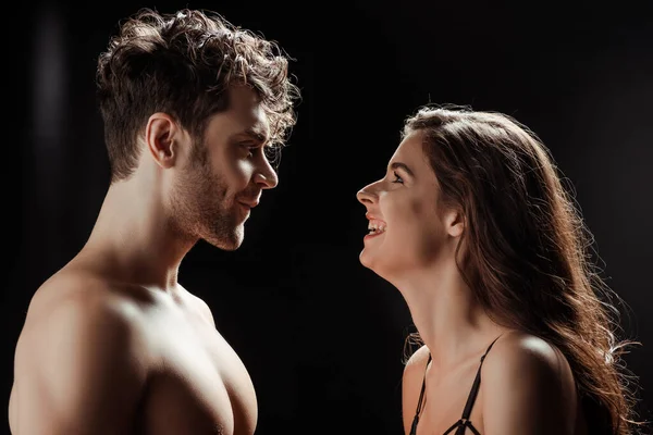 Mujer sonriente mirando al hombre sin camisa sobre fondo negro - foto de stock