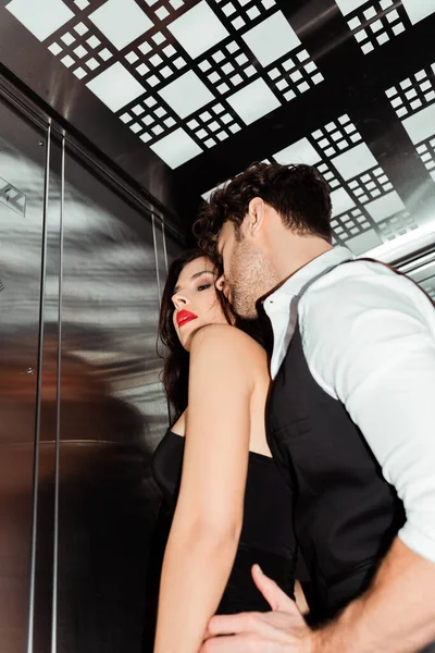 Vista de bajo ángulo del hombre abrazando a mujer seductora con labios rojos en ascensor - foto de stock