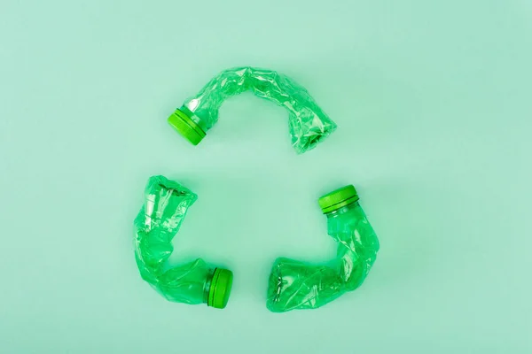 Вид сверху знака переработки из разбитых пластиковых бутылок на зеленом фоне, концепция экологии — стоковое фото