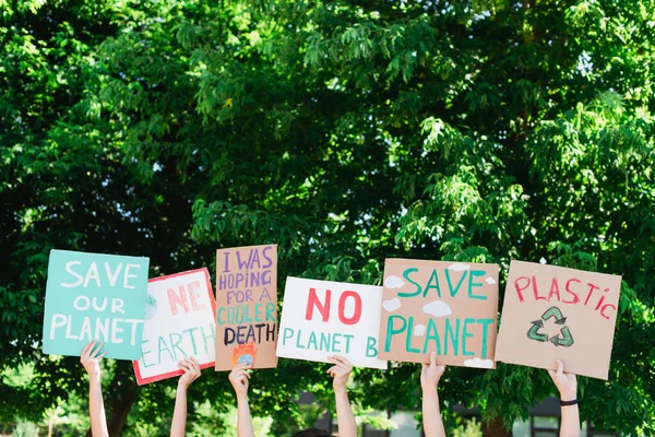 Gente sosteniendo carteles con el planeta de ahorro y plástico reciclar letras con árboles en el fondo, concepto de ecología - foto de stock