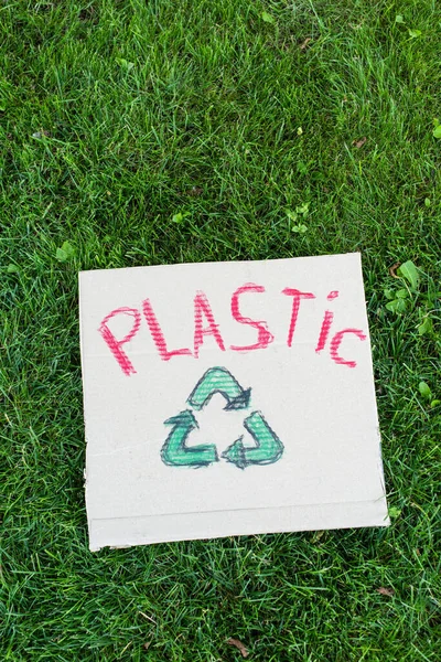 Vue du dessus de la plaque avec lettrage en plastique et panneau de recyclage sur herbe, concept écologique — Photo de stock