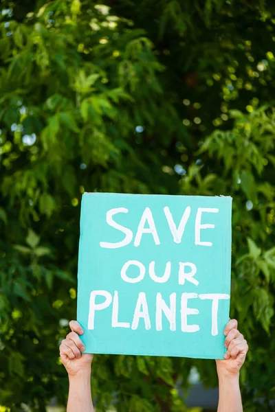 Vista recortada del hombre sosteniendo pancarta con salvar nuestro planeta letras con árboles en el fondo, concepto de ecología - foto de stock