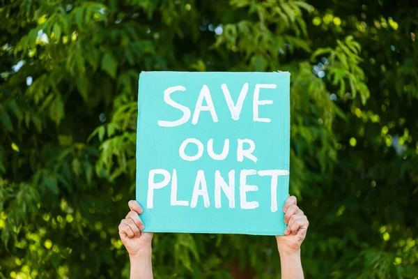 Vista recortada del hombre sosteniendo pancarta con salvar nuestro planeta palabras con árboles en el fondo, concepto de ecología - foto de stock