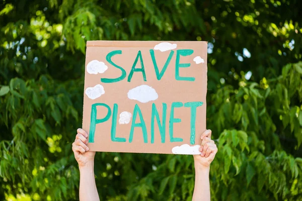 Vista recortada del hombre sosteniendo pancarta con letras de planeta guardado con árboles en el fondo, concepto de ecología - foto de stock