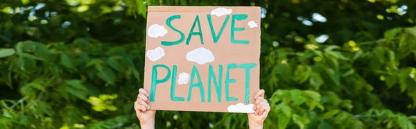 Tiro panorâmico do homem segurando cartaz com salvar planeta lettering com árvores no fundo, conceito de ecologia — Fotografia de Stock