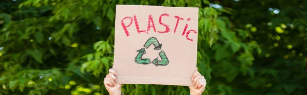 Coltivazione panoramica dell'uomo con cartello con cartello di riciclo e scritte in plastica con alberi sullo sfondo, concetto di ecologia — Foto stock