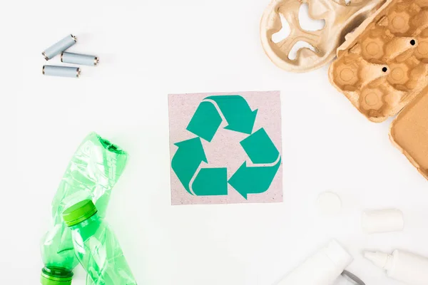 Vista superior de garrafas de plástico, bandeja de ovo de papelão e acumuladores perto de cartão com reciclagem cantar em fundo branco, conceito de ecologia — Fotografia de Stock