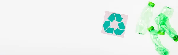 Горизонтальний урожай крихких пластикових пляшок біля картки з символом переробки на білому тлі, концепція екології — стокове фото