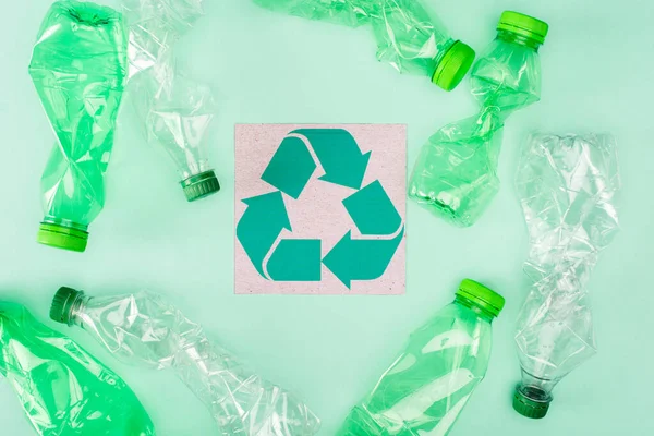 Vista superior do cartão com sinal de reciclagem perto de garrafas amassadas no fundo verde, conceito de ecologia — Fotografia de Stock