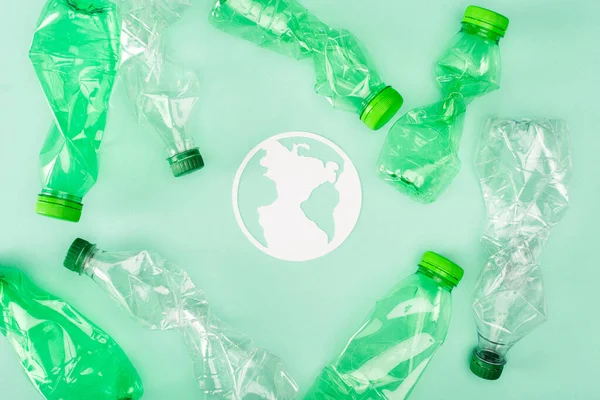 Visão superior do sinal de planeta de papel perto de garrafas de plástico amassadas na superfície verde, conceito de ecologia — Fotografia de Stock
