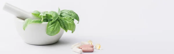 Panoramic shot  of green leaves in mortar near pills on white background, naturopathy concept — Stock Photo