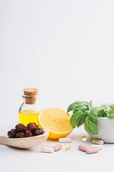 Green leaves in mortar, berries and lemon near pills on white background, naturopathy concept — Stock Photo