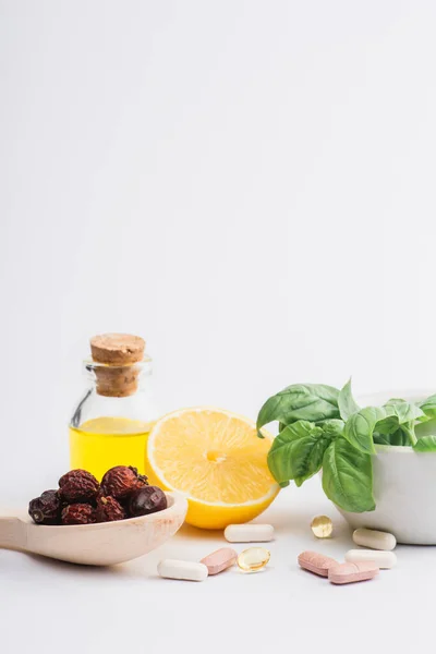 Folhas verdes em argamassa, bagas e limão perto de pílulas em fundo branco, conceito de naturopatia — Fotografia de Stock