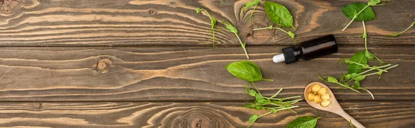 Top view of pills in spoon, green herbs and bottle on wooden surface, naturopathy concept — Stock Photo