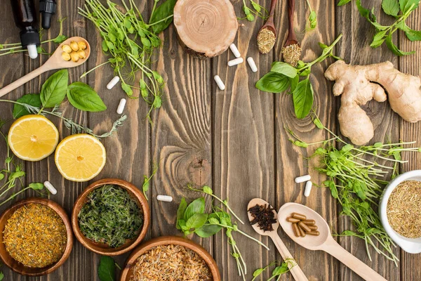 Top view of pills and green herbs on wooden surface, naturopathy concept — Stock Photo