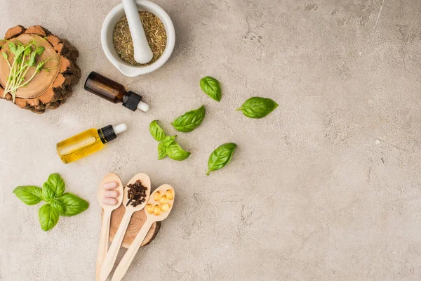 Top view of herbs, green leaves, mortar with pestle, bottles and pills in wooden spoons on concrete background, naturopathy concept — Stock Photo