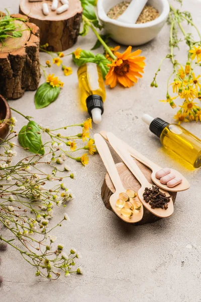 Focus selettivo di fiori di campo, erbe, bottiglie e pillole in cucchiai di legno su sfondo concreto, concetto di naturopatia — Foto stock