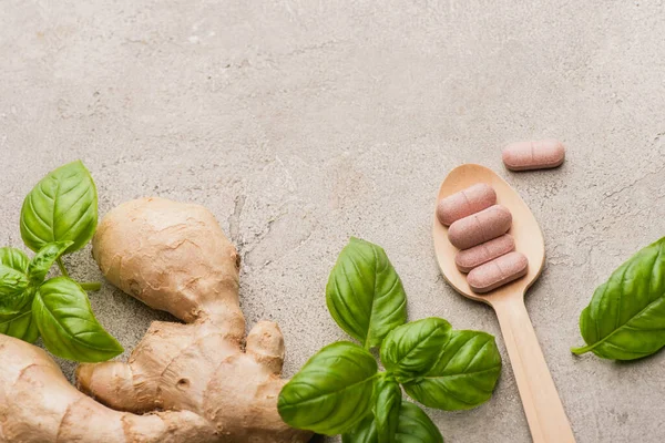 Top view of green leaves, ginger root and pills in wooden spoon on concrete background, naturopathy concept — Stock Photo