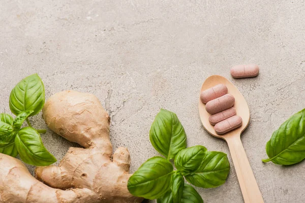 Vista dall'alto di foglie verdi, radice di zenzero e pillole in cucchiaio di legno su sfondo concreto, concetto di naturopatia — Foto stock